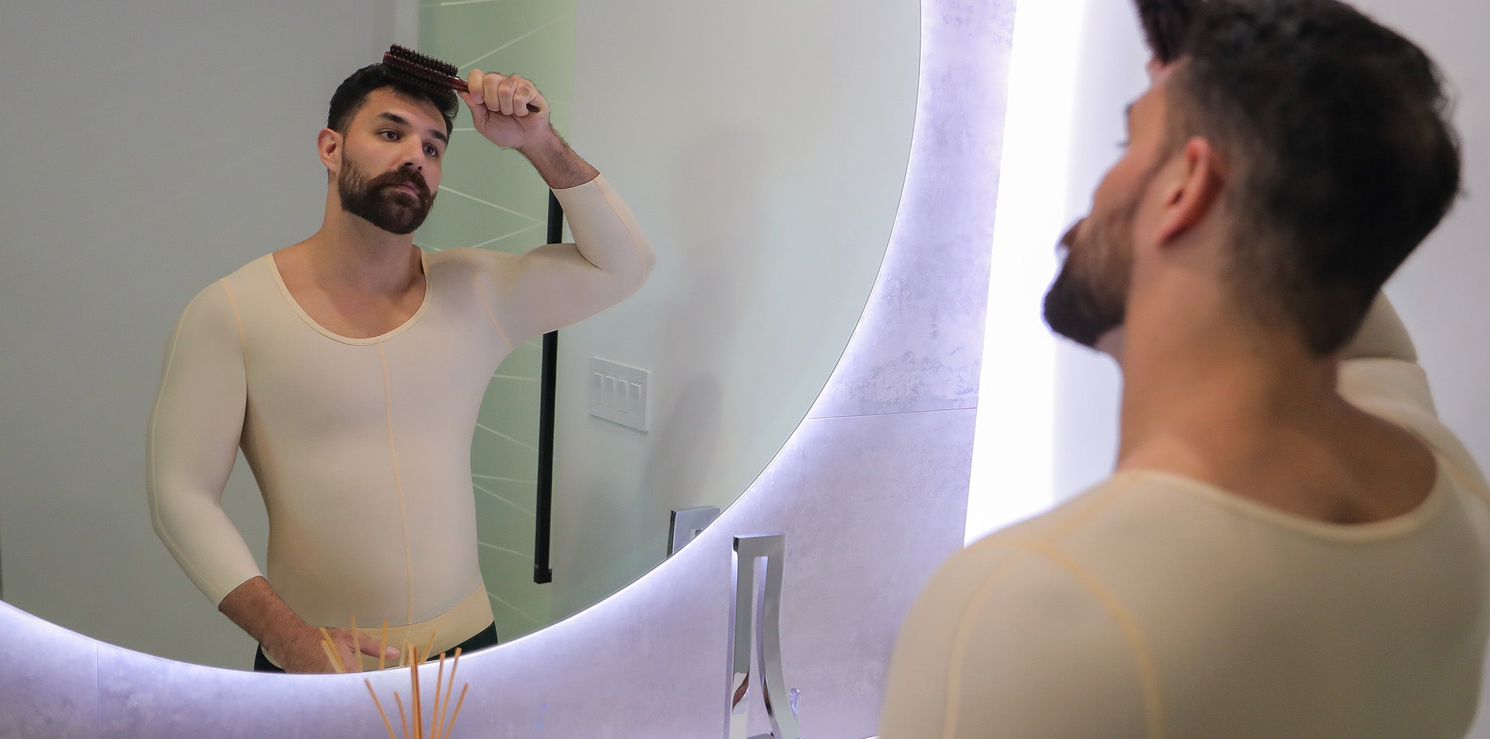 Man wearing beige compression garment combing his hair in front of a mirror