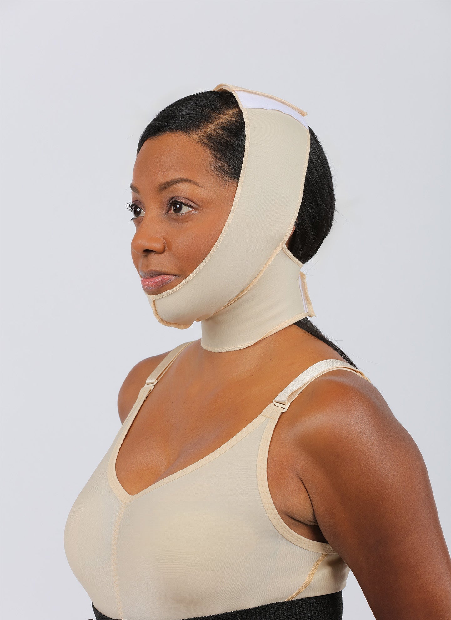 Female model in beige compression garment and face wrap, side profile